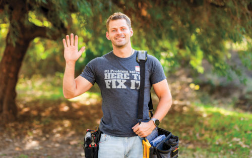 Efim Kostylev stands in a park with a bag belt and tools, waving.
