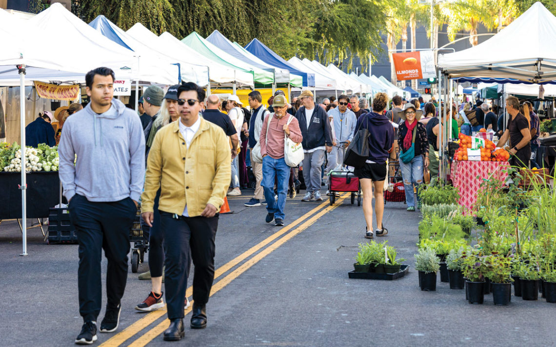 Shoppers walk between stands at a farmers market.
