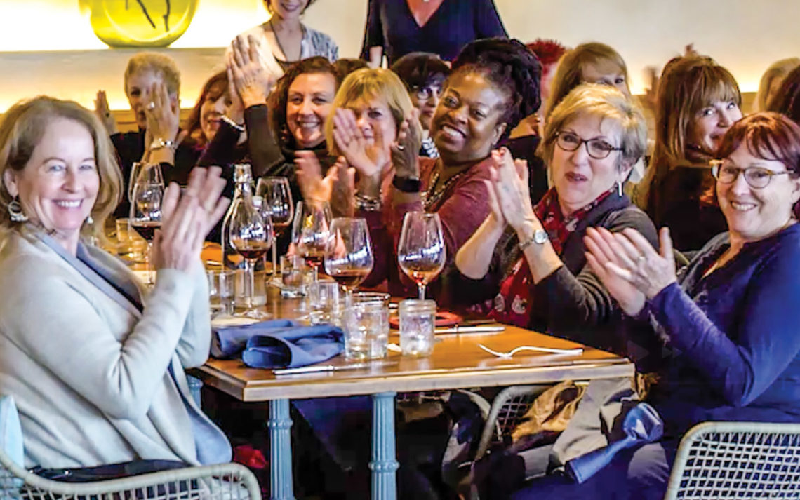 Members of Finding Female Friends Past 50 clap at a dinner table